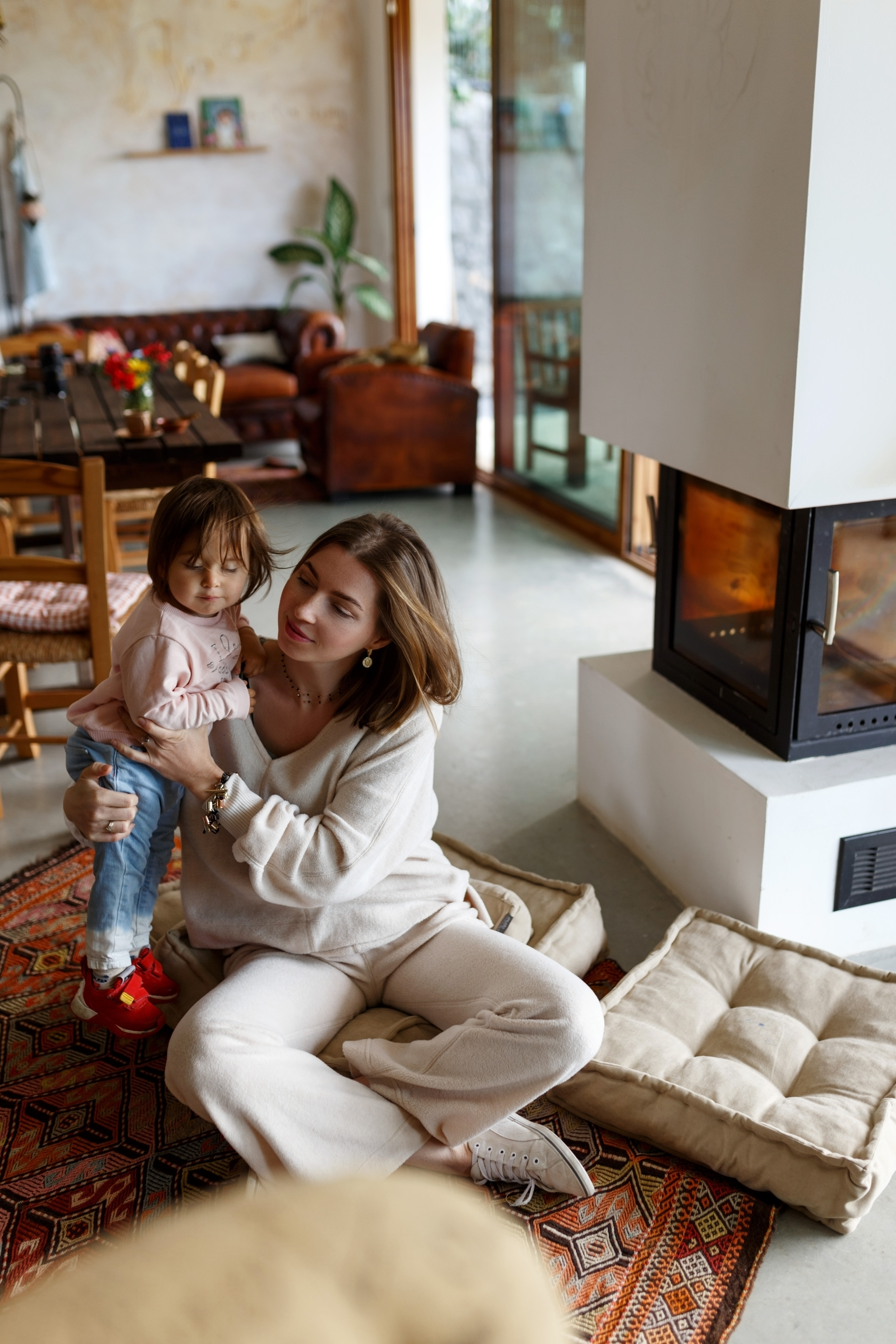 Happy young mother and toddler daughter spending time together on floor near fireplace at home